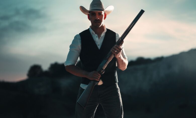 A cowboy in traditional attire holding a shotgun, standing outdoors in San Antonio, Texas.