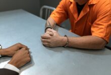 Close-up of prisoner in orange uniform handcuffed during an interrogation.