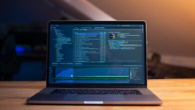 A laptop displaying code on a wooden desk, in a dimly lit workspace.