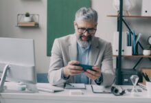 Senior businessman smiling while using smartphone at office desk.