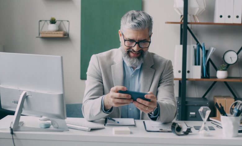 Senior businessman smiling while using smartphone at office desk.