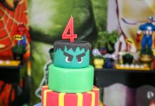 Two-tier superhero themed birthday cake topped with a number four candle, perfect for children's parties.