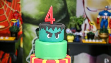 Two-tier superhero themed birthday cake topped with a number four candle, perfect for children's parties.