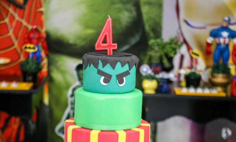 Two-tier superhero themed birthday cake topped with a number four candle, perfect for children's parties.