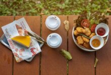 Top view of outdoor picnic table with fast food, sauce dips, and two beverage cups.