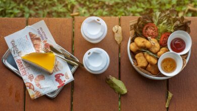 Top view of outdoor picnic table with fast food, sauce dips, and two beverage cups.