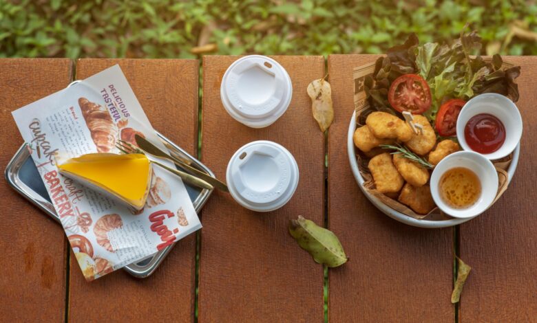 Top view of outdoor picnic table with fast food, sauce dips, and two beverage cups.