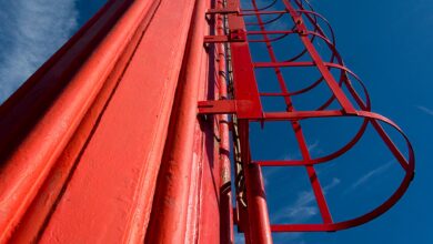 Dramatic low angle view of a red metal ladder on an industrial chimney against a clear blue sky.