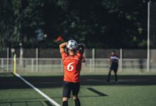 Focused soccer player in red jersey preparing to throw the ball during a match on a sunny day.