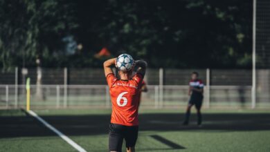 Focused soccer player in red jersey preparing to throw the ball during a match on a sunny day.