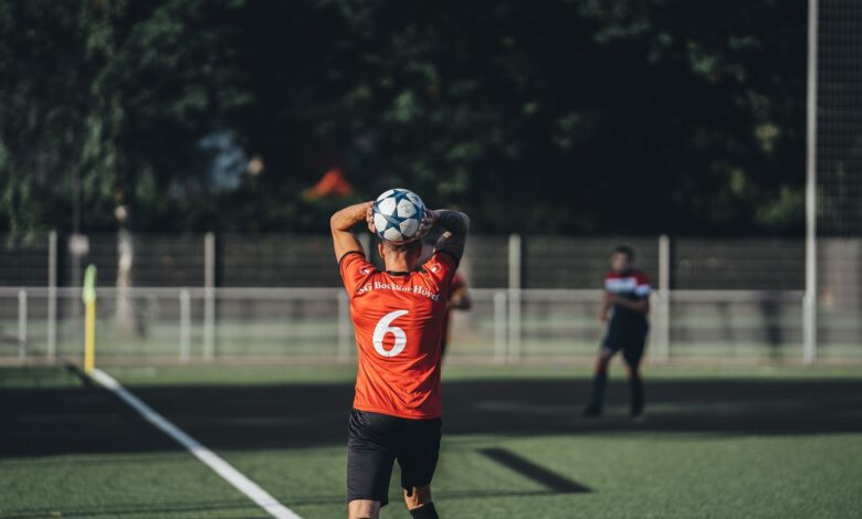 Focused soccer player in red jersey preparing to throw the ball during a match on a sunny day.