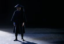 Dramatic studio portrait of a person in a dark costume with shadowed lighting.