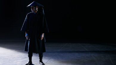 Dramatic studio portrait of a person in a dark costume with shadowed lighting.