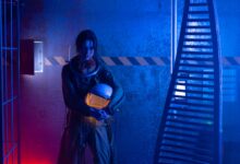 A female astronaut holding a helmet in a dramatic, futuristic setting with blue and red lighting.