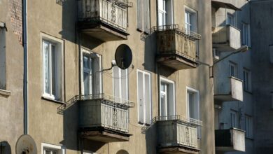Exterior view of an apartment building with balconies and satellite dishes in sunlight.