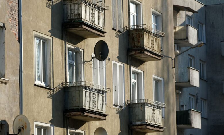 Exterior view of an apartment building with balconies and satellite dishes in sunlight.