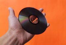 Close-up of a hand holding a classic compact disc with an orange background, evoking nostalgia.