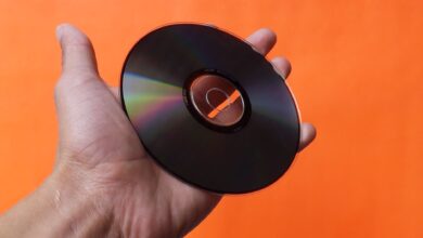 Close-up of a hand holding a classic compact disc with an orange background, evoking nostalgia.