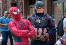 Spider-Man and Captain America cosplayers pose in a lively street scene with onlookers.