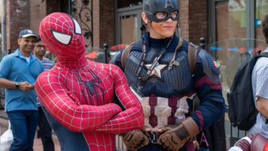 Spider-Man and Captain America cosplayers pose in a lively street scene with onlookers.