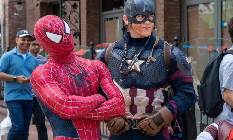 Spider-Man and Captain America cosplayers pose in a lively street scene with onlookers.