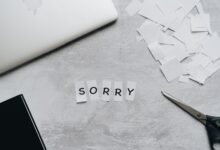 Top view of a desk with cut-out letters spelling 'sorry', scissors, and a laptop.