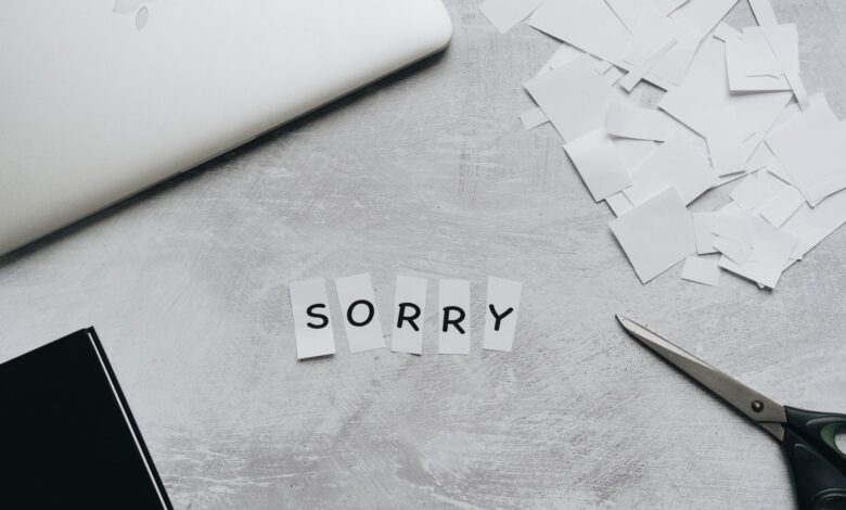 Top view of a desk with cut-out letters spelling 'sorry', scissors, and a laptop.