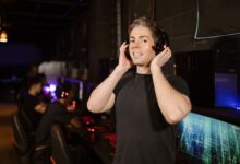 A man in a black shirt with headphones, enjoying gaming in a cyber cafe.