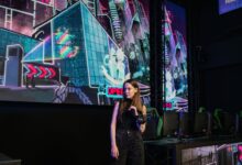 A woman stands in a virtual reality gaming arena with vibrant neon backdrops, wearing casual attire.