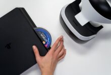 Close-up of a hand inserting a VR World's disc into a PlayStation with VR headset nearby.