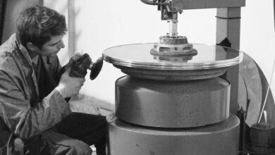 A concentrated worker polishes a large metal disc in an industrial setting.