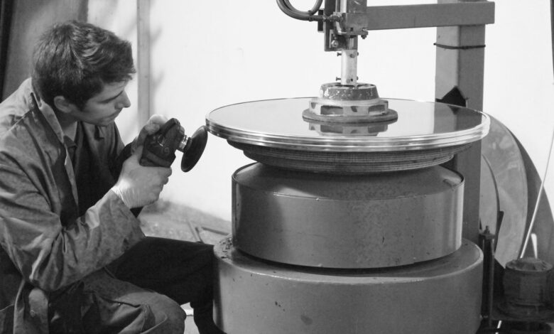 A concentrated worker polishes a large metal disc in an industrial setting.