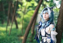 A cosplayer dressed in a blue themed costume poses in a lush forest.