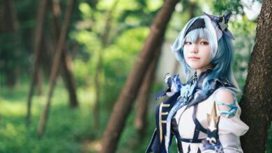 A cosplayer dressed in a blue themed costume poses in a lush forest.
