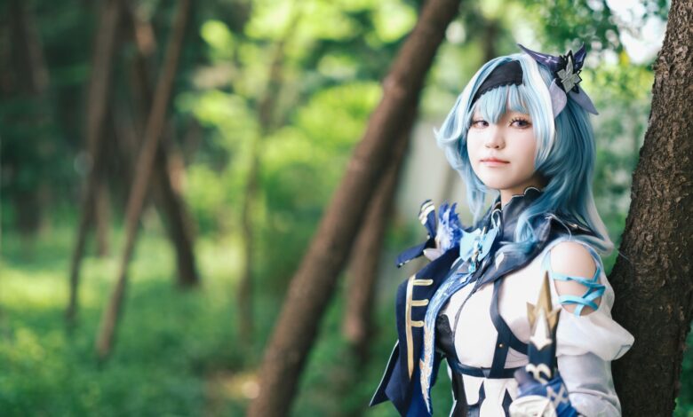 A cosplayer dressed in a blue themed costume poses in a lush forest.