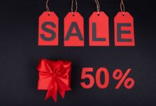 Red gift box next to sale tags and 50% sign on black background, ideal for promotions.