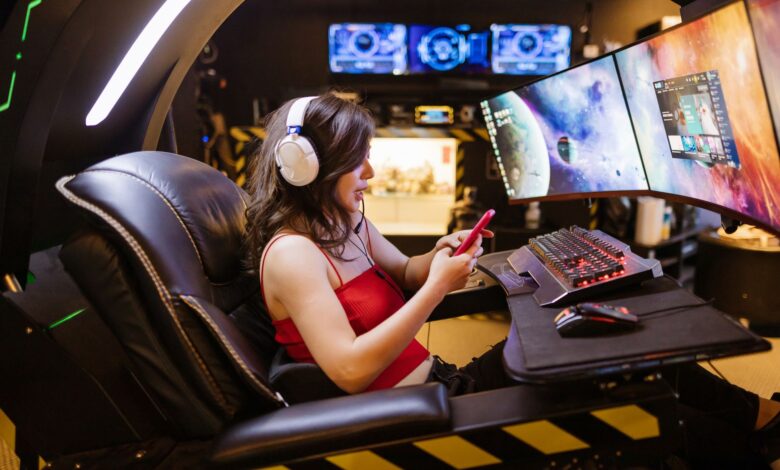 Young woman enjoying computer gaming at home with a high-tech gaming setup and smartphone.