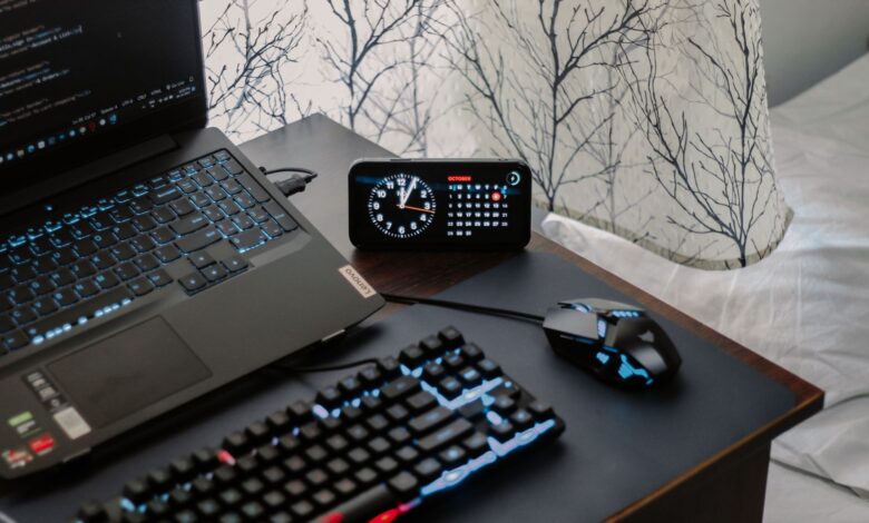 A modern workspace featuring a laptop, digital clock, gaming mouse, and keyboard, ideal for work and tech enthusiasts.