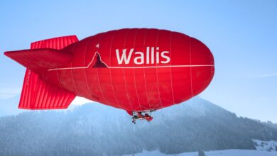 Bright red airship flying over snowy mountains in Château-d’Œx, Switzerland, with clear blue skies.