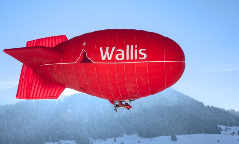 Bright red airship flying over snowy mountains in Château-d’Œx, Switzerland, with clear blue skies.
