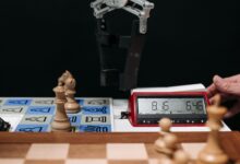 Robotic arm moves chess pieces on a board with electronic digital timer displayed.
