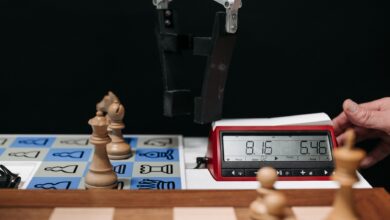 Robotic arm moves chess pieces on a board with electronic digital timer displayed.