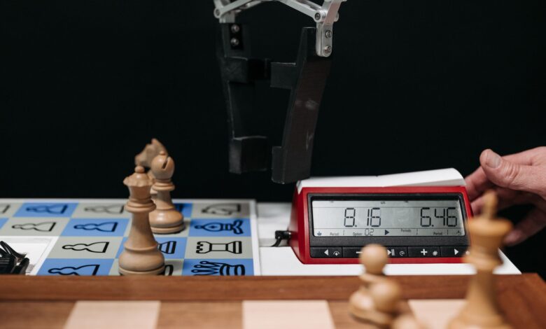 Robotic arm moves chess pieces on a board with electronic digital timer displayed.
