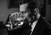 Black and white image of a man sipping whiskey, evoking classic film noir style.