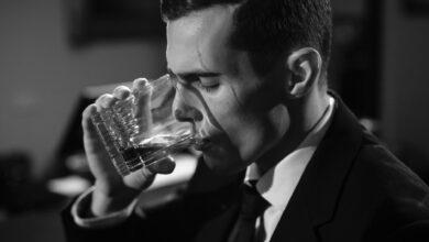 Black and white image of a man sipping whiskey, evoking classic film noir style.