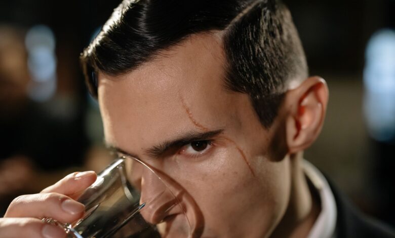 Close-up of a mysterious scarred man holding a glass, creating a noir atmosphere.