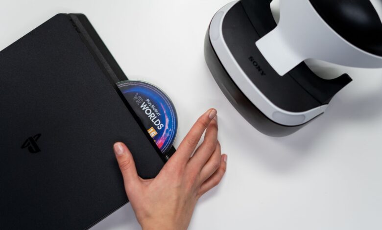 Close-up of a hand inserting a VR World's disc into a PlayStation with VR headset nearby.