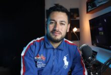 Man in a blue jacket with microphone recording a podcast in a home studio setup.