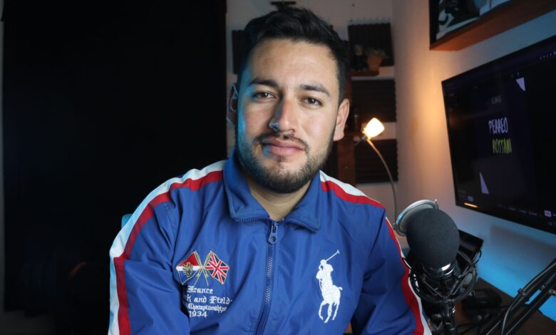 Man in a blue jacket with microphone recording a podcast in a home studio setup.