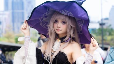 A young woman cosplaying as a witch outdoors, wearing a purple hat and fantasy attire.